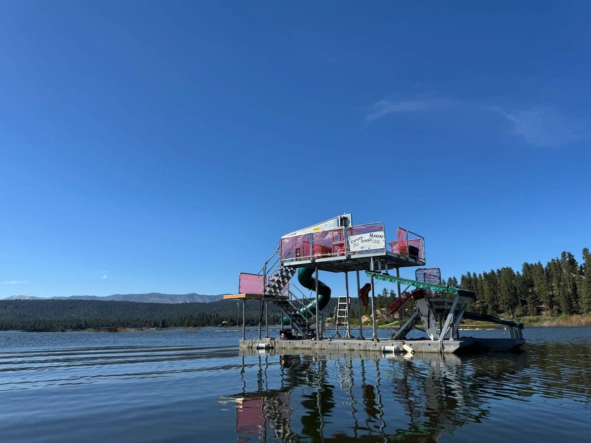 The Tarzan Jungle Float anchored on calm water, its two-story slide and jumping platforms reflected below.