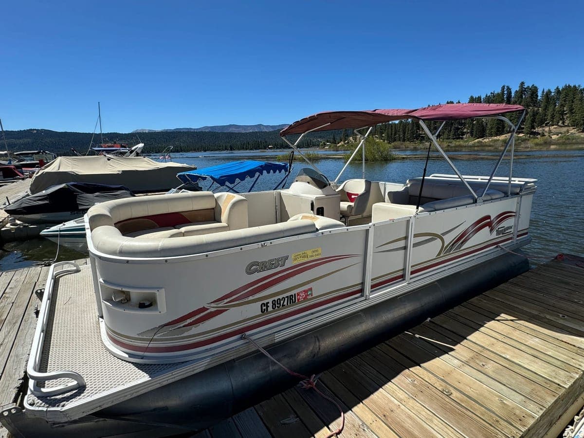 A classic pontoon boat tied at the dock with the lake and pine ridge behind it.